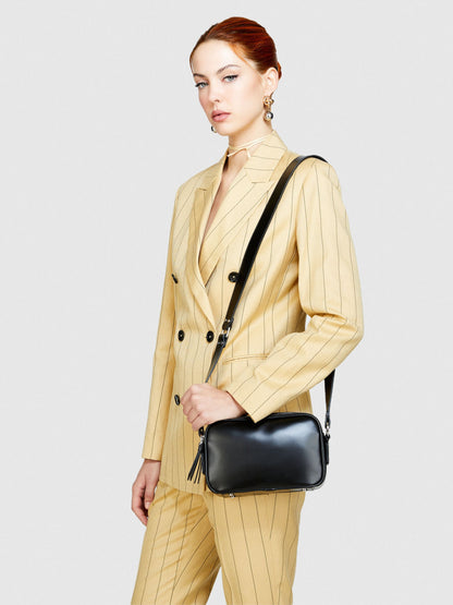 Female model wearing a black leather camera bag or messenger bag crossbody, paired with a stylish striped suit, showcasing a complete outfit.