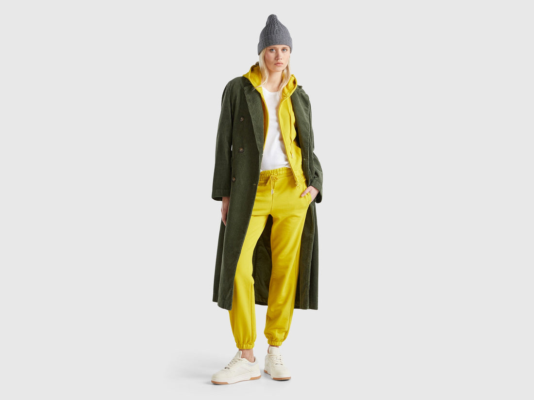 Female model wearing yellow drawstring sweatpants, paired with a green coat and grey beanie, showcasing a winter casual outfit.