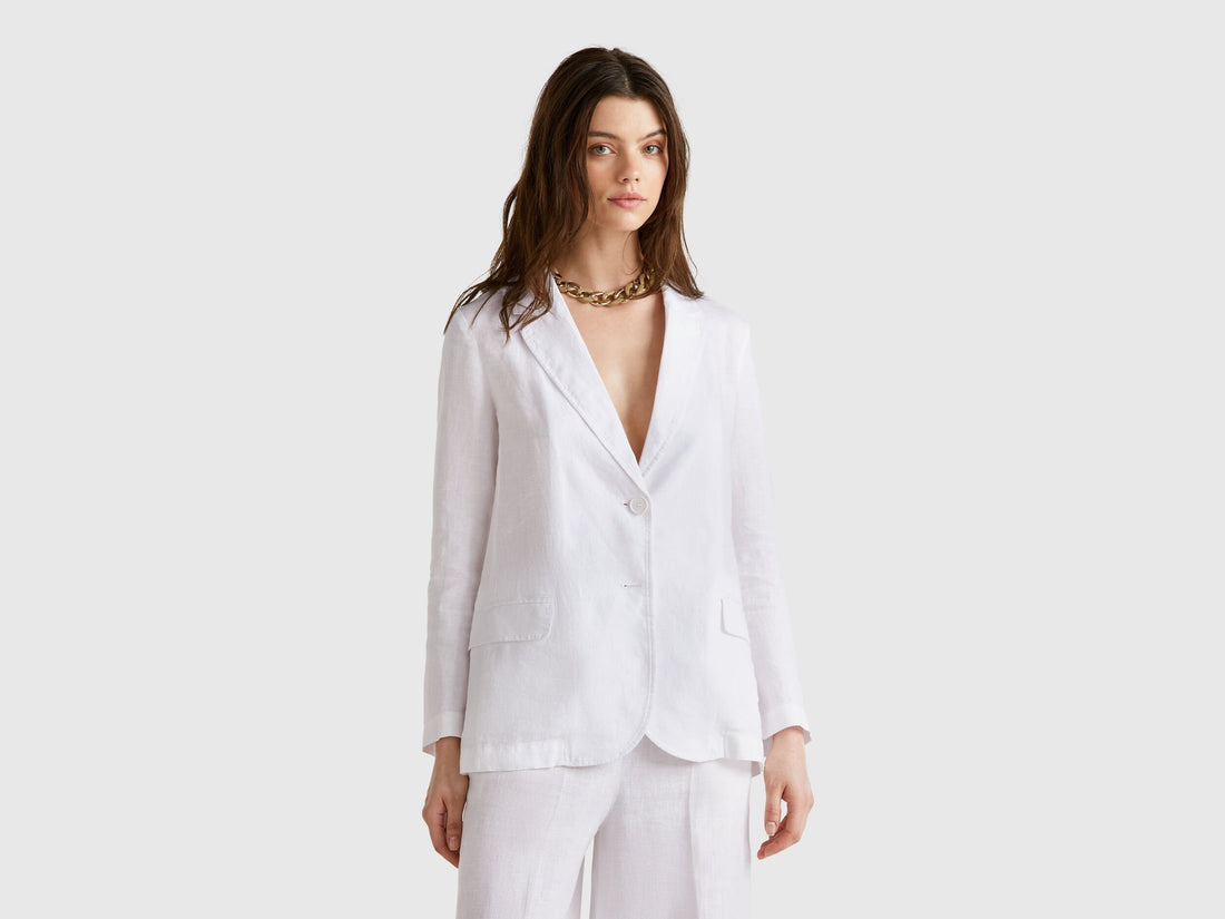 Female model wearing a white pure linen Benetton blazer with matching wide-leg pants, in a relaxed, elegant pose.
