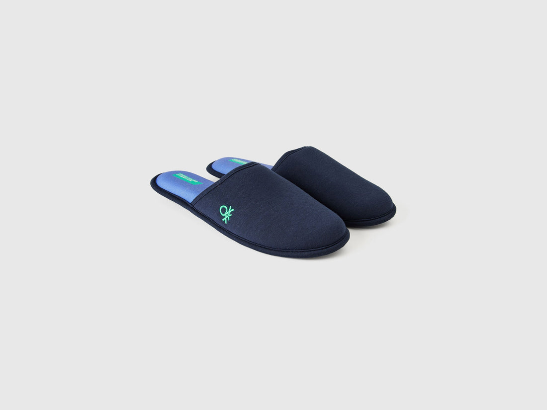 Angled view of a pair of navy blue slippers with a green logo.