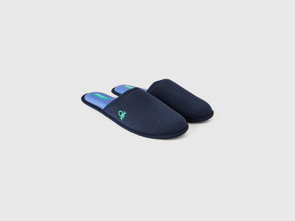 Angled view of a pair of navy blue slippers with a green logo.