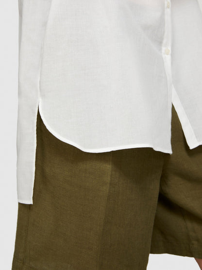Close-up of the rounded hem of an oversized white shirt over khaki shorts.