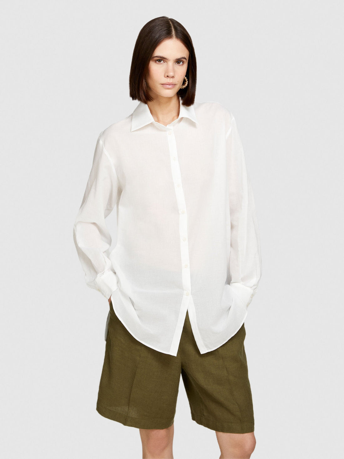 Front view of a model wearing an oversized white shirt, khaki shorts, and a black bucket hat.