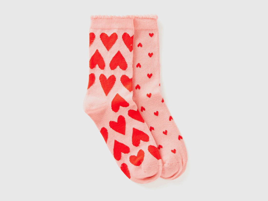 Pair of light pink long socks with all-over red heart pattern, ideal for women.