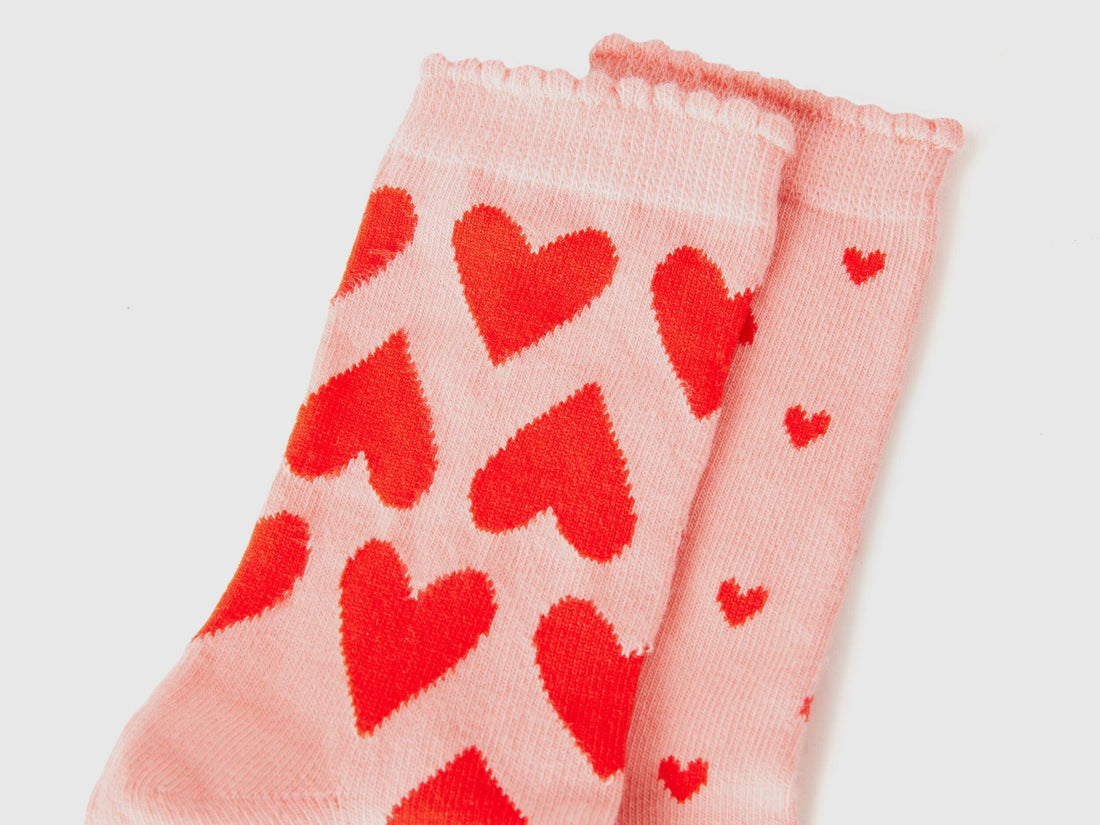 Close-up of light pink long socks with vibrant red heart pattern. Soft knit texture.