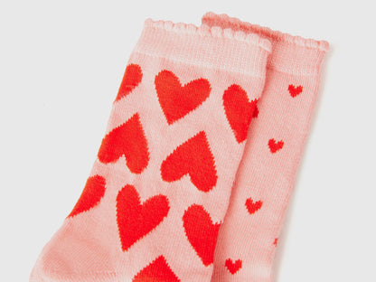 Close-up of light pink long socks with vibrant red heart pattern. Soft knit texture.