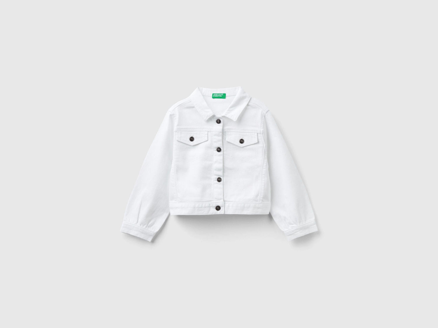 Front view of a white cropped jacket in stretch cotton denim, featuring silver buttons and a classic collar.