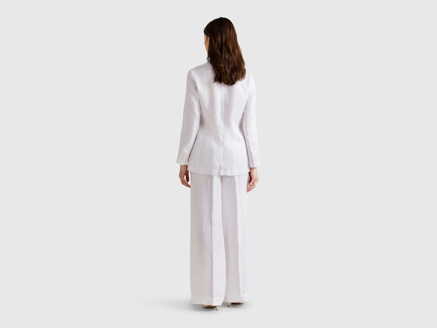 Close-up of a white pure linen Benetton blazer worn by a model, featuring a gold chain necklace and showcasing the blazer&