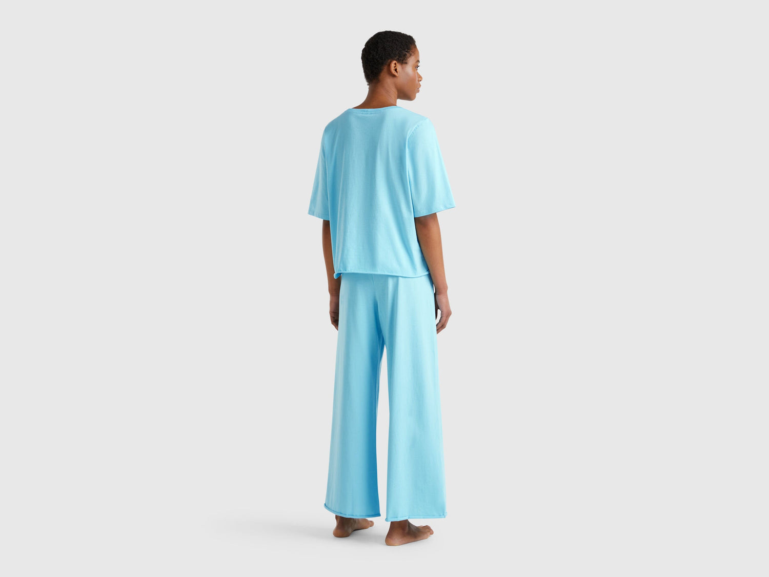  Back view of a woman wearing a light blue loose-fitting pyjama set.