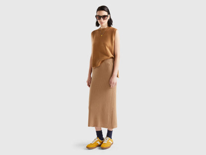 Full body shot of a woman in a light brown knit vest, matching skirt, sunglasses, and yellow shoes.