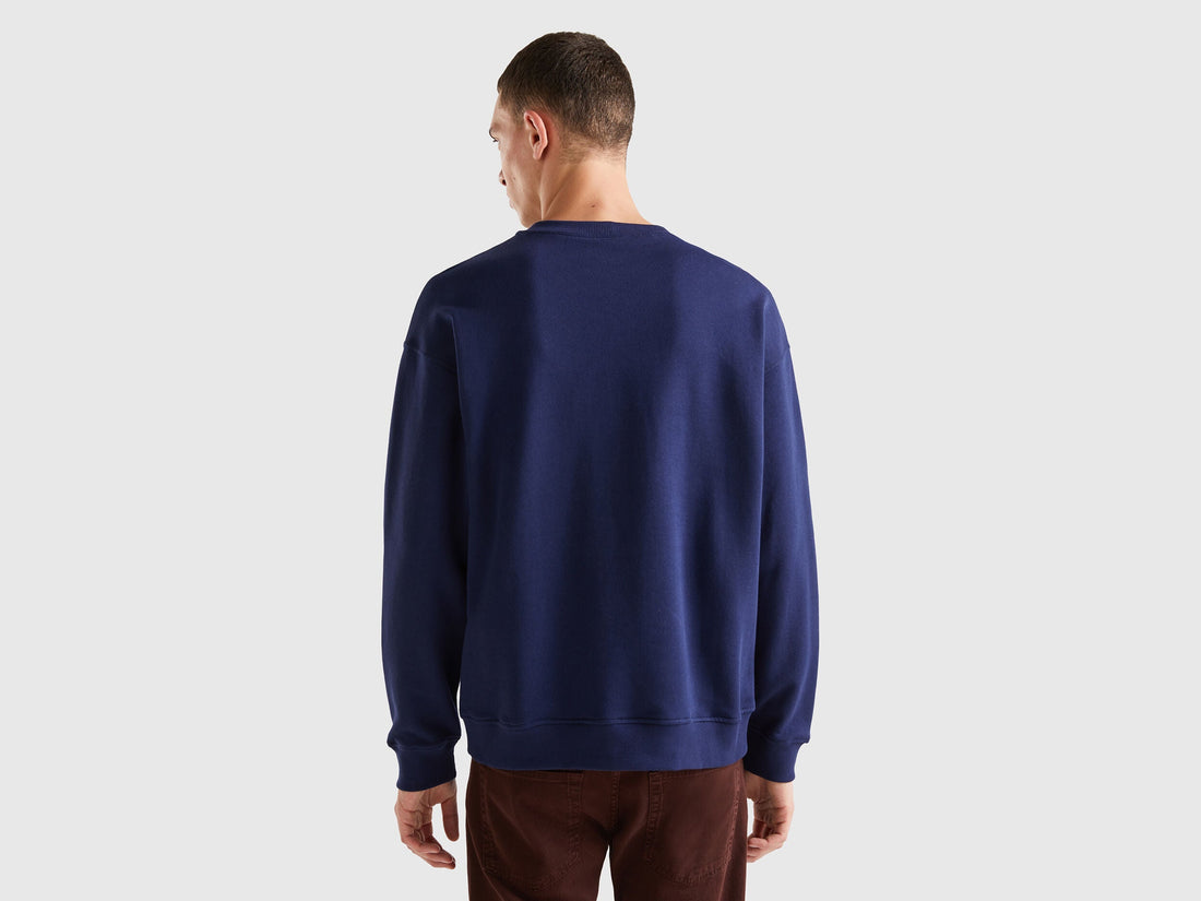 Back view of a man wearing a plain blue crew neck sweatshirt.