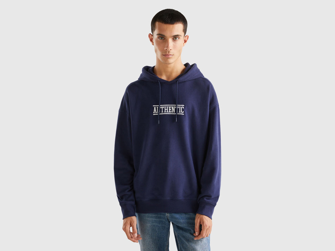 Front view of a man wearing a blue hoodie with a white &quot;BENETTON&quot; logo and graphic print.