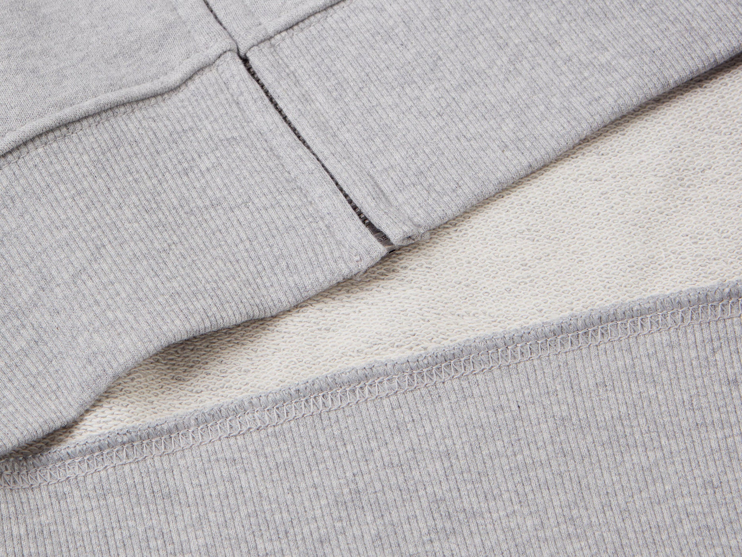 Close-up of the zipper on a grey cotton zip-up hoodie, showing the ribbed hem.