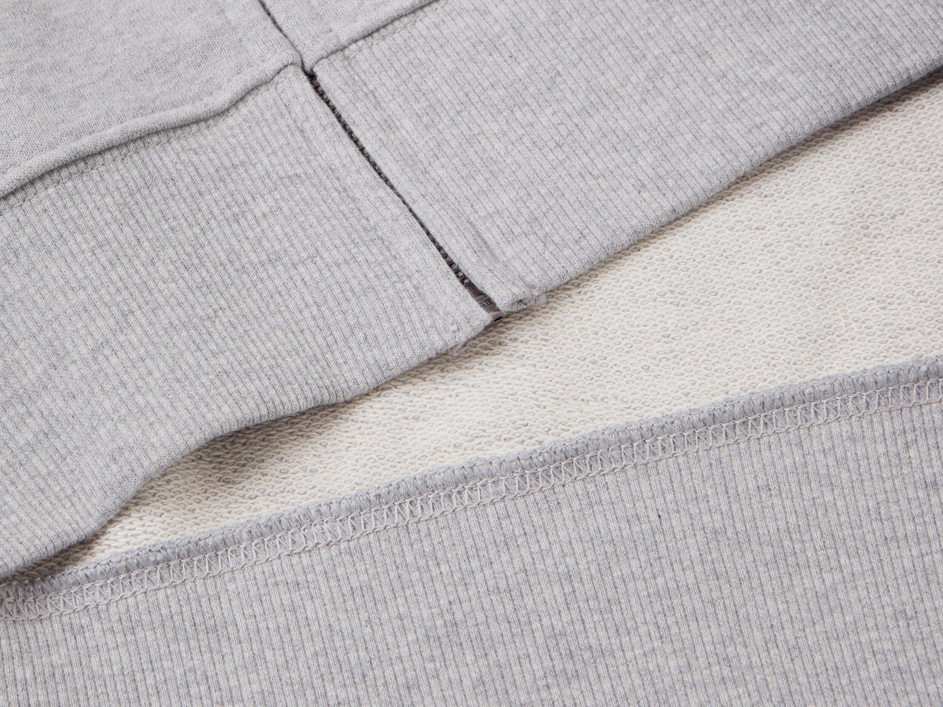 Close-up of the zipper on a grey cotton zip-up hoodie, showing the ribbed hem.