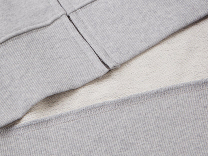 Close-up of the zipper on a grey cotton zip-up hoodie, showing the ribbed hem.