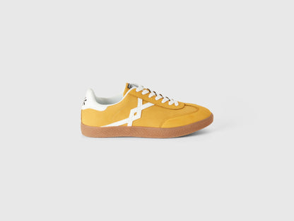 Single mustard yellow low-top sneaker with white stripe.