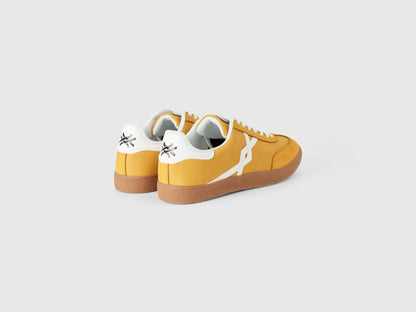 Angled back view of mustard yellow low-top sneakers.