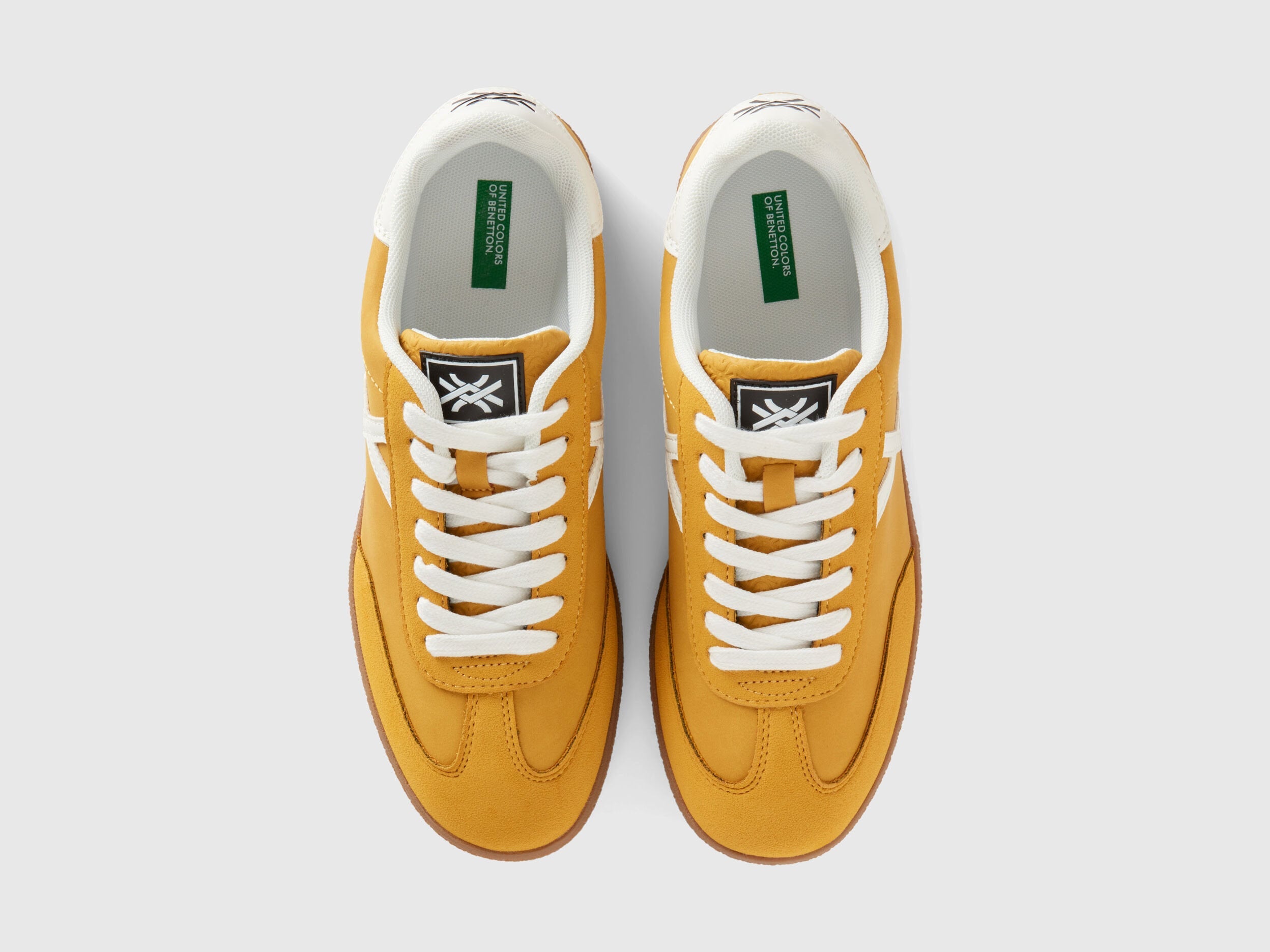  Top view of a pair of mustard yellow low-top sneakers with white laces.