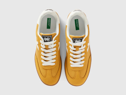 Top view of a pair of mustard yellow low-top sneakers with white laces.