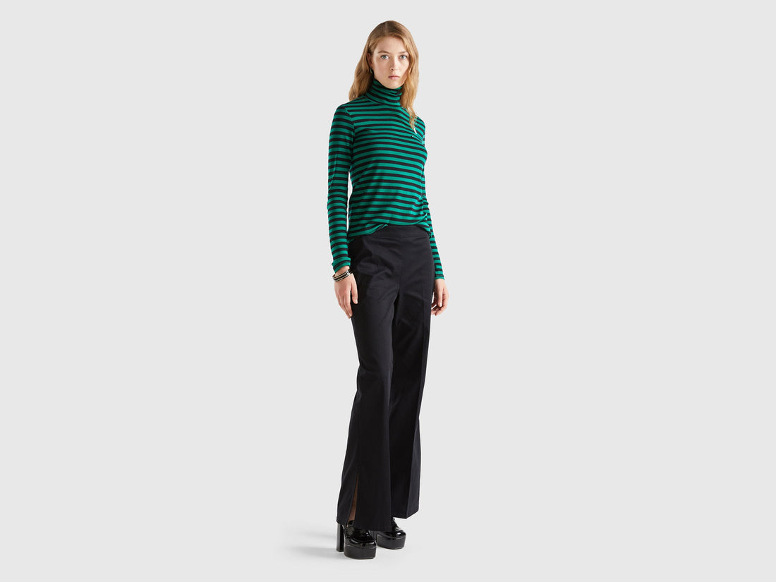 Front view of a woman wearing black flared pants and a striped green top.