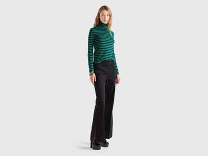  Front view of a woman wearing black flared pants and a striped green top.